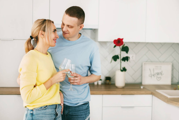 Romantik genç bir çift ellerinde kadehlerle modern bir mutfakta, yıldönümünü ya da sevgililer gününü birlikte kutluyorlar. - Fotoğraf, Görsel