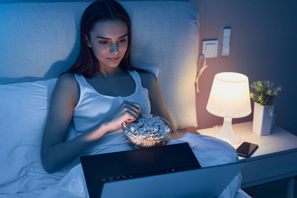 Female with popcorn watching move on bed - Foto, imagen