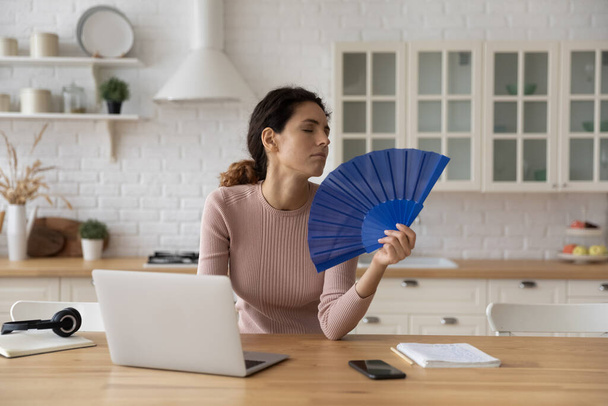Woman feels overheated cools herself with hand fan - 写真・画像