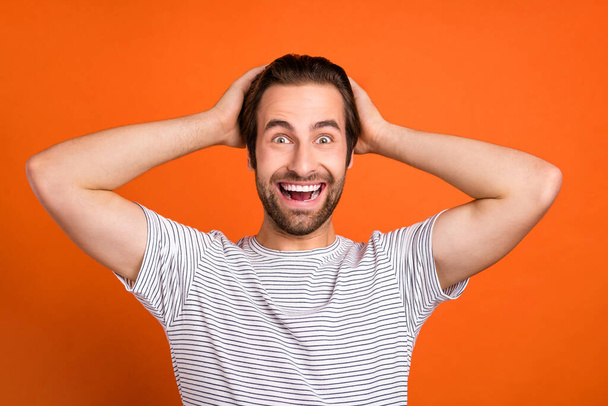 Photo of young man good mood arms touch head impressed good news isolated over orange color background - Foto, immagini