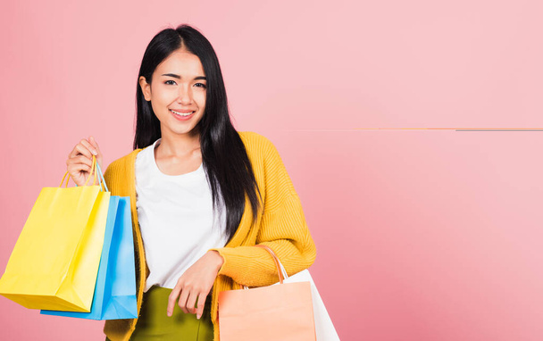 Portrait of Asian happy beautiful young woman teen shopper smiling standing excited holding online shopping bags colorful multicolor in summer, studio shot isolated on pink background with copy space - Fotó, kép