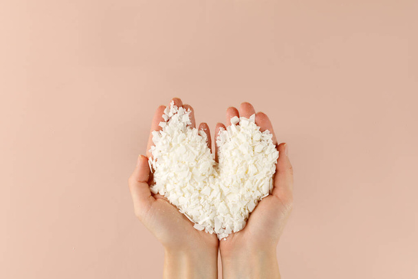 Hand with organic white Soy wax flakes for candles and sachet. Heart. Flatlay, top view. Natural soy and coconut wax for candlemaker. - Fotografie, Obrázek