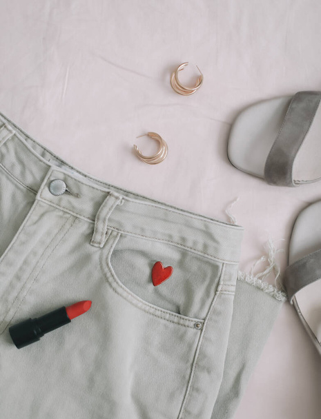 Jeans, sandals and red lipstick on beige background. Overhead view of womans casual spring summer outfit. Trendy stylish women clothes. Flat lay, top view - Foto, Imagem