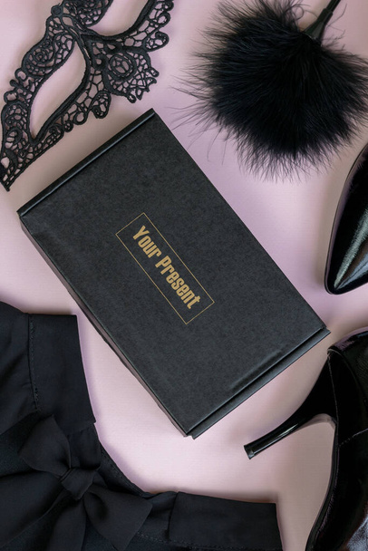 Creatieve compositie met een zwart kanten masker voor vrouwen, jurk, bont en een geschenkdoos op een roze achtergrond. Het concept van een preasent. - Foto, afbeelding