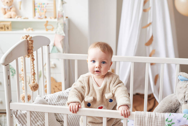 Baby 6 months standing in crib in children's room. Happy motherhood and fatherhood. Maternity hospital and clinic. Father and mother day. Early childhood development, nursery. - Фото, зображення