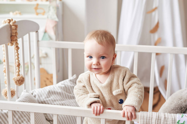 Baby 6 months standing in crib in children's room. Happy motherhood and fatherhood. Maternity hospital and clinic. Father and mother day. Early childhood development, nursery. - Fotoğraf, Görsel