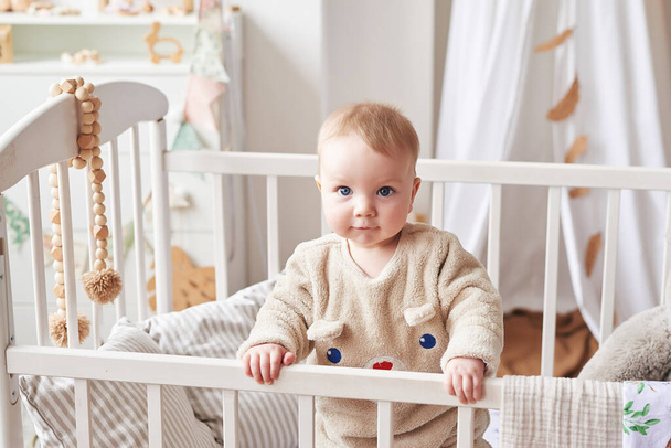 Baby 6 months standing in crib in children's room. Happy motherhood and fatherhood. Maternity hospital and clinic. Father and mother day. Early childhood development, nursery. - Fotoğraf, Görsel