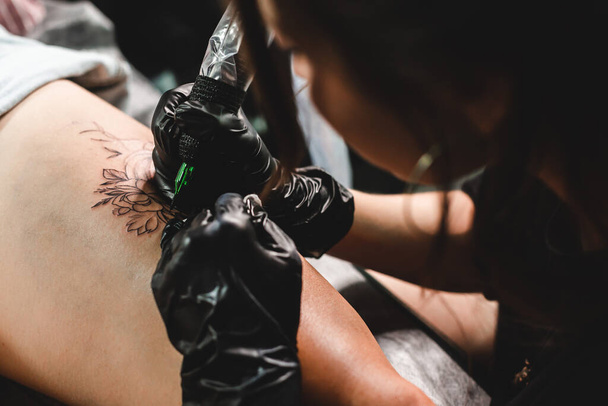 A professional tattoo artist makes a black and white tattoo on a womans leg, applying in ink. The process of tattooing the skin. - Zdjęcie, obraz