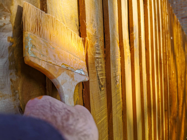 Paing orange appliqué sur une clôture en bois avec un pinceau au début du printemps. processus de nettoyage. - Photo, image