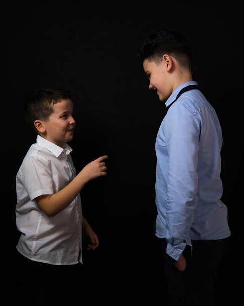 Two boys on a black background are brothers.Senior and junior.Atelier.proof.hands in pockets - Foto, Imagem