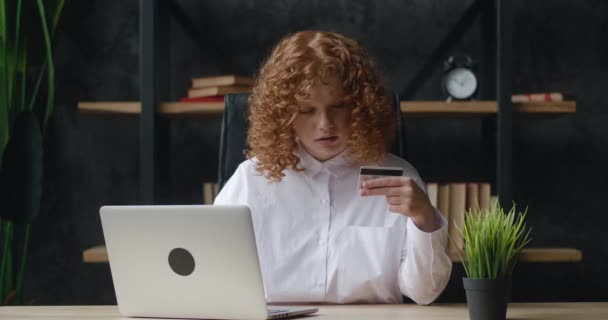 Hübsches rothaariges Mädchen macht Online-Zahlung mit Bankkarte mit modernem Laptop am Bürotisch sitzend und lächelnd. Finanzen, Einkaufen im Internet und Jugendkonzept. - Filmmaterial, Video