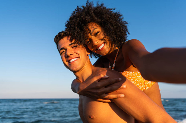 Positive fun self portrait of young traveling couple in love - having fun on amazing tropical beach - Happy traveling couple making selfie - sunny summer colors - romantic mood - happy couple at the beach - piggyback ride - Foto, Imagen