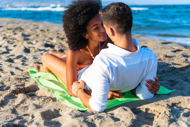 multiraciální šťastný pár na pláži, ležící na sobě - Letní radostný koncept a multietnický pár - Sunny odpolední barevné tóny se zaměřením na dívku držící fotoaparát. - Fotografie, Obrázek