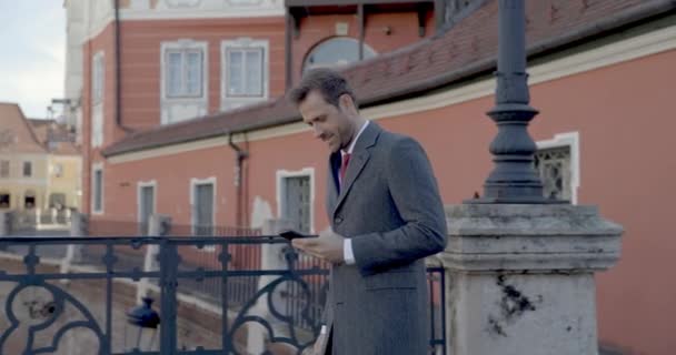 видео проекта элегантный мужчина отвечает на телефон, имеющие разговор, ходьба, оглядываясь назад и улыбаясь на улице - Кадры, видео