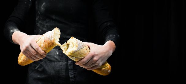 Women's hands break the baguette. Isolated on black background. - Foto, afbeelding