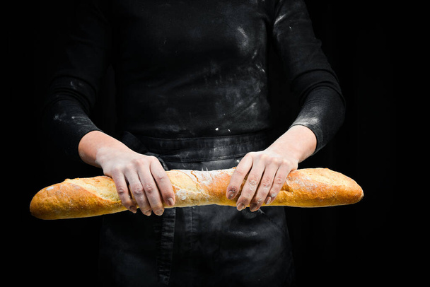 Fragrant fresh baguette in hands. Black cooking background. Isolated on black background. - Foto, afbeelding