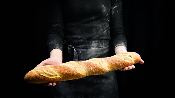 Fragrant fresh baguette in hands. Black cooking background. Isolated on black background. - Photo, Image