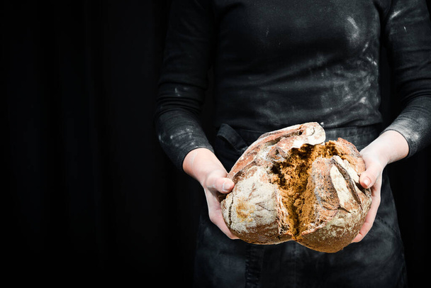 Hands break black bread from flour. Black cooking background. Isolated on black background. - Fotografie, Obrázek