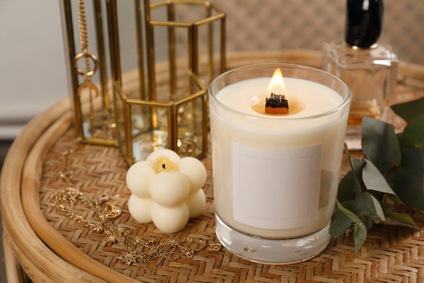 Burning soy candle, perfume and stylish accessories on wicker table indoors - Photo, image
