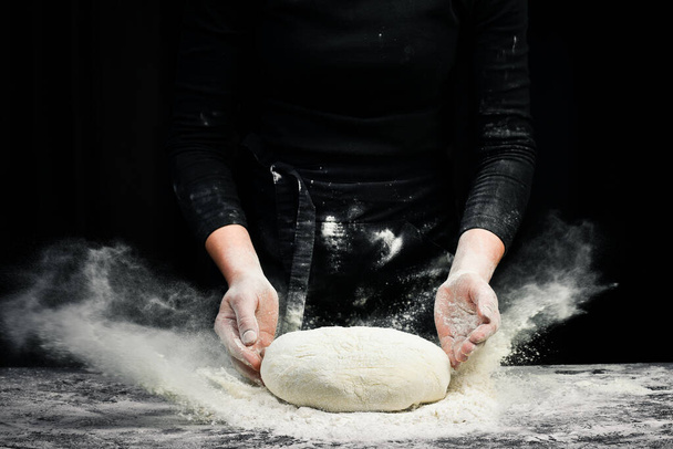 Cooking dough by chef hands for homemade pastry bread with flour splash. On a dark background. - Foto, Imagen