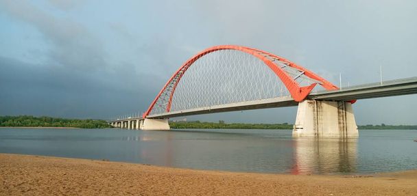 Красная арка кабельного подвесного моста через широкую реку Оби. Новосибирск, Россия. - Фото, изображение