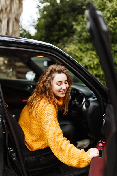 Portrait of young beautiful woman in yellow sweater sitting in the car - Foto, Imagen
