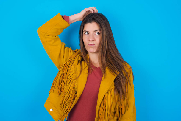 young beautiful woman wearing jacket over blue studio background saying: Oops, what did I do? Holding hand on head with frightened and regret expression. - Foto, afbeelding