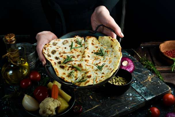 Pita bread with rosemary, Jewish matsa on a plate in the hands of a chef On a black background. - Photo, Image