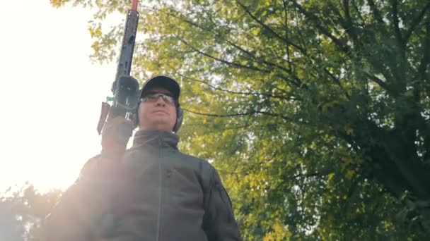 Retrato de un cazador masculino con un arma de caza lisa en sus manos con auriculares y gafas. - Metraje, vídeo