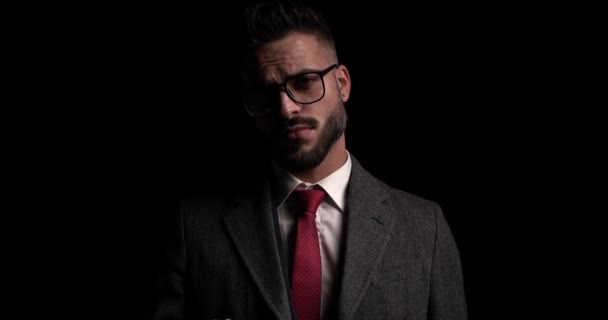 joven hombre de negocios mirando a la cámara con actitud, arreglando sus gafas y abrigo - Imágenes, Vídeo