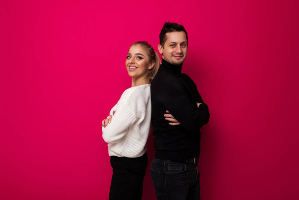 Photo of a beautiful pretty amazing positive smiling happy young blonde woman with makeup and ponytail in a stylish white knitted sweater and black pants and an adult brunet man with stubble in a - Photo, Image