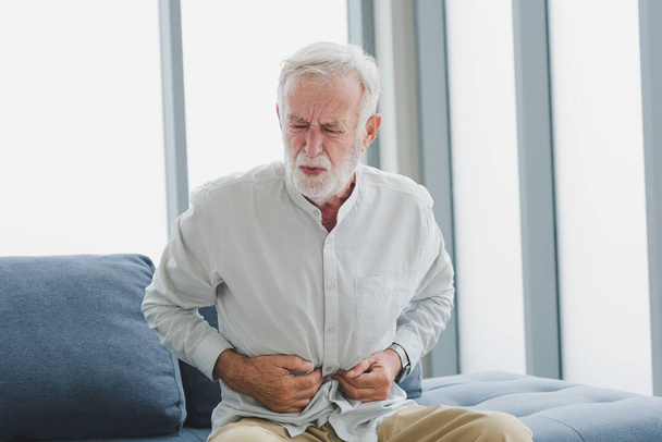 Senior elderly man in casual outfit get stomachache with unhappy and painful emotion in modern living room. - Foto, imagen