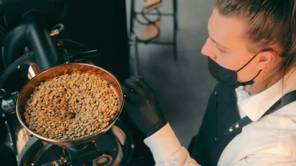 焙煎されていない生のコーヒー豆が自動コーヒーロースターに注ぎ込まれます。コーヒーロースターに生のコーヒー豆を充填. - 映像、動画