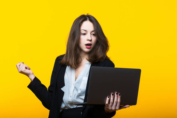 Portrait of a young woman in a business suit with a laptop on a yellow background - Foto, imagen