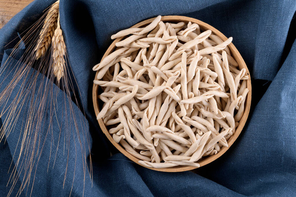 Ціле зерно пшениці апулії Pizzarieddi або Maccaruni в сито на блакитній лляній серветці. Свіжі макхерони, типова страва Пульї Саленто в Італії. Італійська домашня макарони тло, вид зверху рівний - Фото, зображення