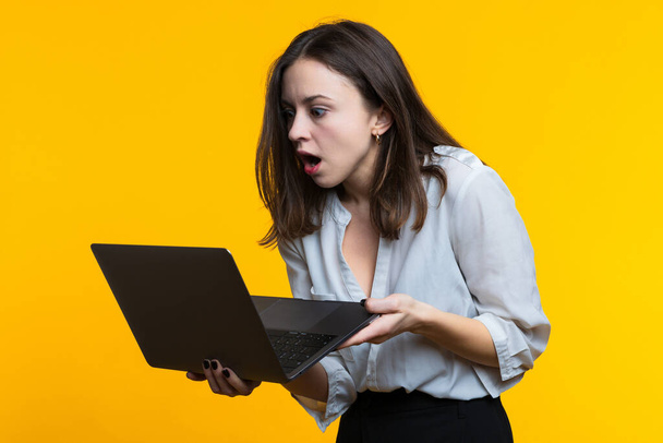 A young woman in a white shirt holds a laptop on a yellow background - Fotoğraf, Görsel