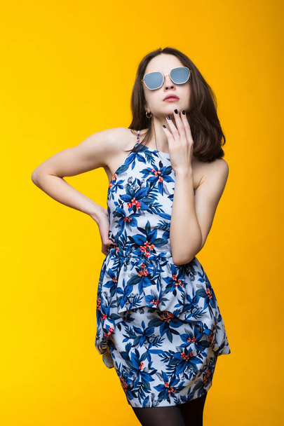 Atraktivní mladá žena v šatech a sluneční brýle na žlutém pozadí - Fotografie, Obrázek