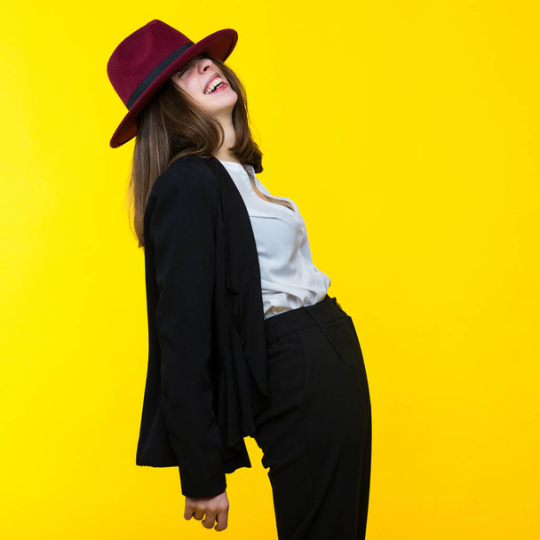 A young woman in a suit and hat dancing on a yellow background - Photo, image