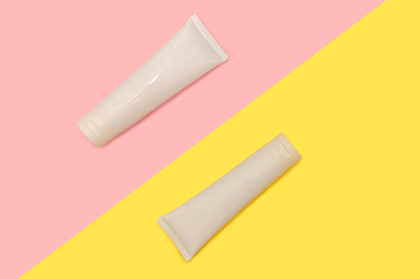 Two white plastic containers for cream. On a pink and yellow background. - Photo, image
