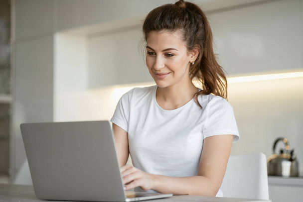 a woman is typing sitting at home in the kitchen at a laptop com - Foto, Bild