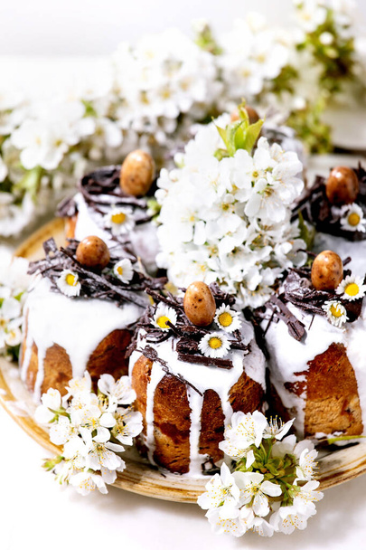 Homemade traditionla Easter cake with chocolate nests and eggs on ceramic plate and blossoming cherry tree over white background. Traditional ortodox Easter Russian Ukrainian bake. Close up - Photo, image