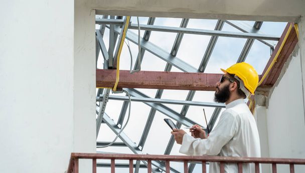 A hagyományos egyenruhába és biztonsági sisakba öltözött közel-keleti arab mérnökök lakásépítési projekteket vizsgálnak.. - Fotó, kép