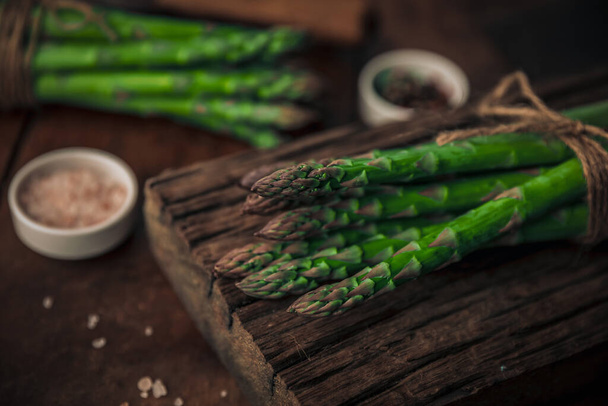 lovely fresh asparagus bunch of top of an old very textured wood chopping board, vintage overall look on a rustic table - 写真・画像