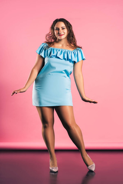 Happy plus size model in blue dress on pink background, body positive concept - Фото, зображення