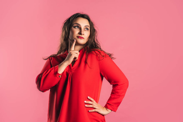 Doubting plus size model in red dress on pink background, body positive concept - Valokuva, kuva