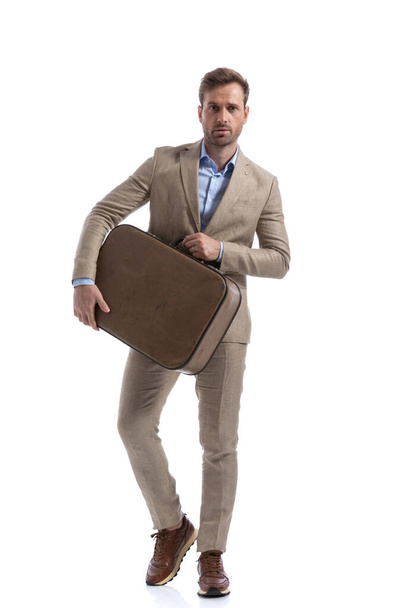 hombre casual inteligente posando con un maletín en sus manos y mirando a la cámara contra el fondo blanco - Foto, Imagen