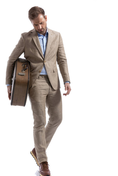 dramático hombre de negocios mirando hacia abajo mientras camina y sostiene un maletín sobre fondo blanco - Foto, imagen