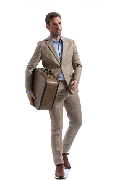 fiatal jóképű üzletember kezében a táskát, miközben séta és pózol a fehér háttér - Fotó, kép