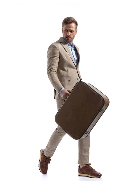 handsome businessman walking one way and looking the opposite while holding a briefcase against white background - Zdjęcie, obraz