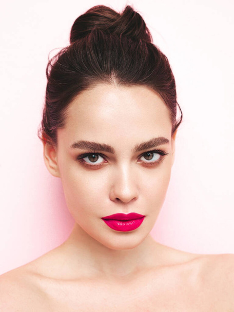 Fashion beauty portrait of young brunette woman with evening stylish  makeup and perfect clean skin. Sexy model with hair in a bun posing in studio near white wall. With pink bright natural lips - Фото, зображення